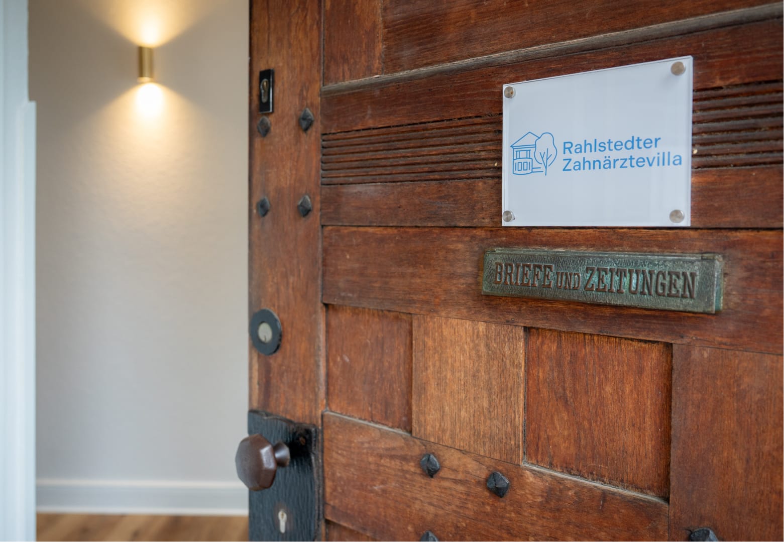 Nahaufnahme der Eingangstür der Rahlstedter Zahnärztevilla mit Praxisschild mit Logo
